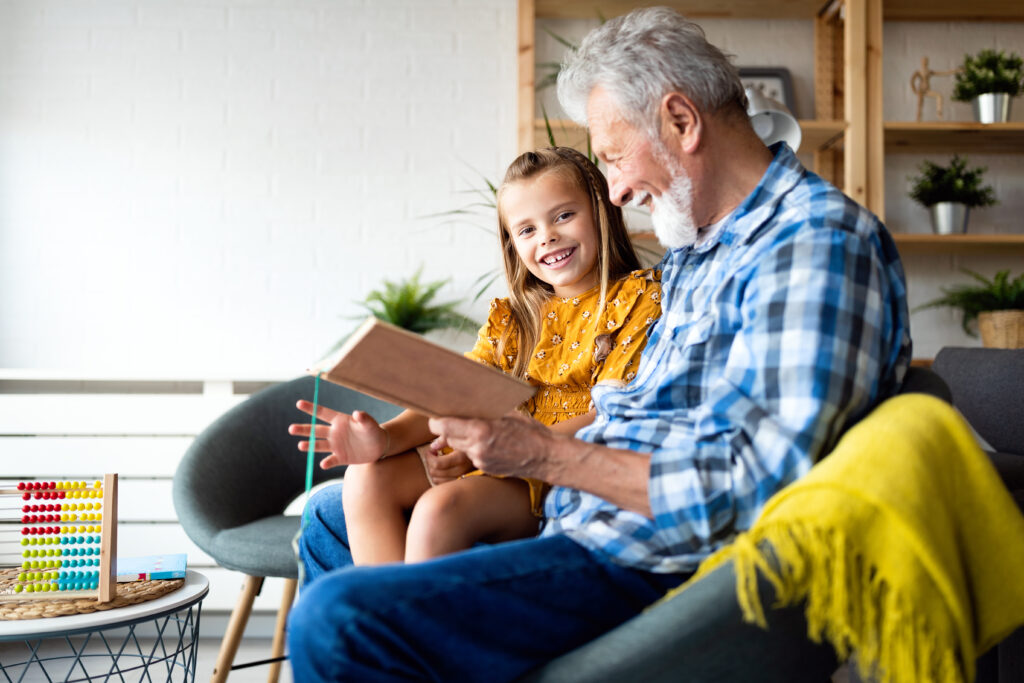 Happy little girl with grandfather reading story book at home