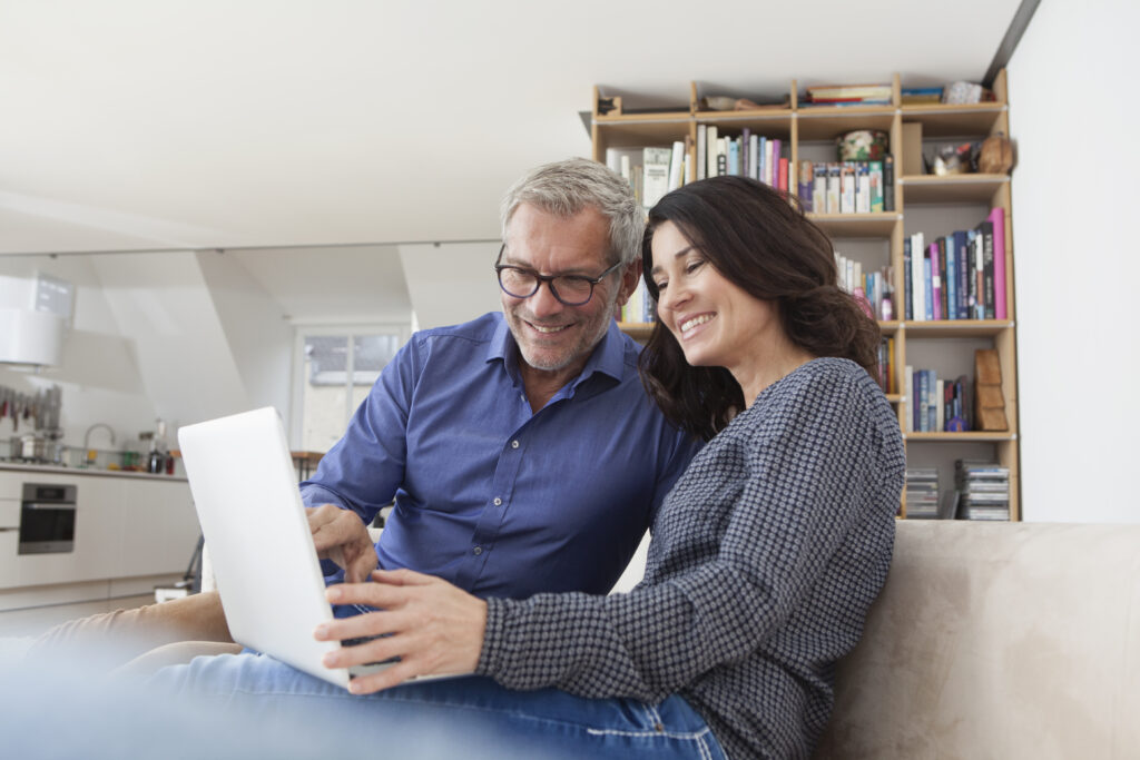 Smiling couple at home on couch using laptop